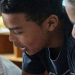 Three middle school age students talk together in a classroom.